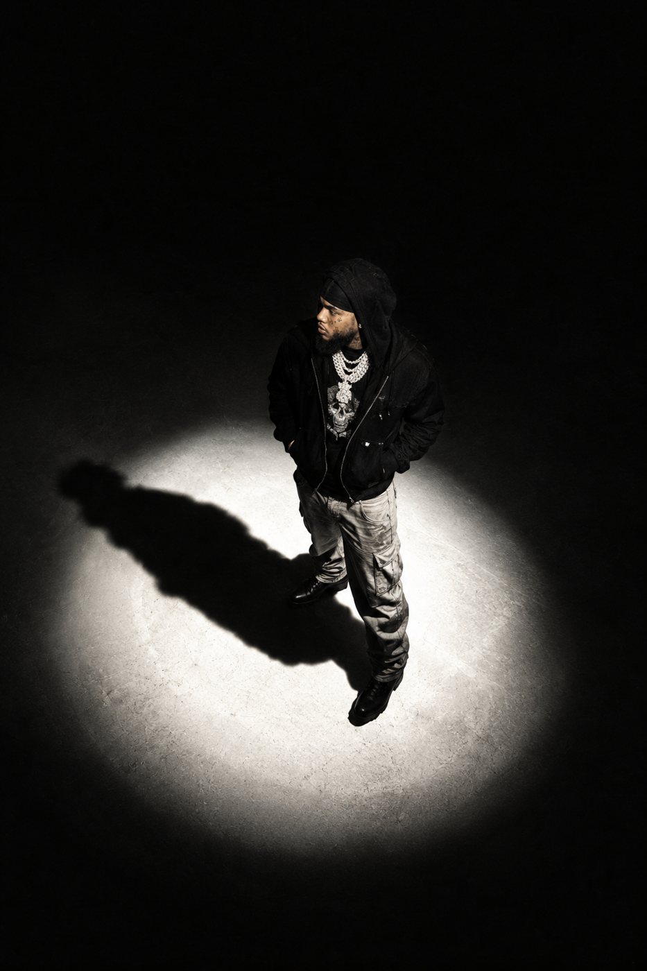 Overhead spotlight portrait of a man in black standing in a circle of light